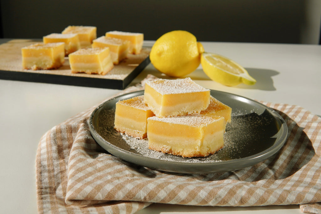 Image of a plate filled with tangy Lemon Bars baked using Selo Croatian Extra Virgin Olive Oil, dusted with powdered sugar and garnished with fresh lemon zest.
