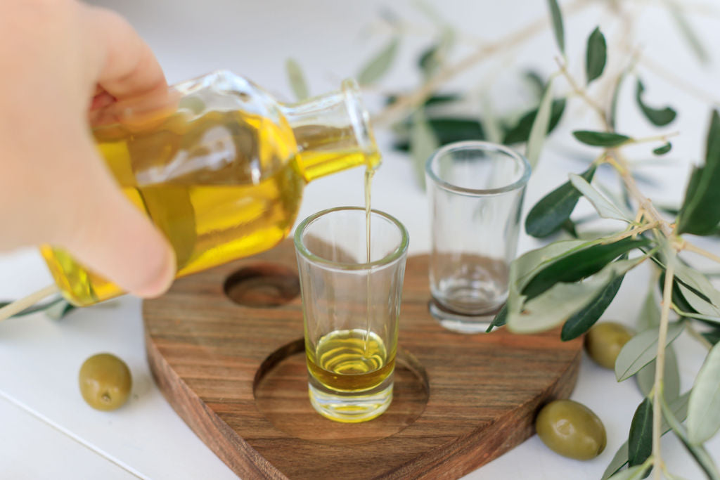 Vibrant young woman savoring pure olive oil from a glass amidst a sun-drenched olive orchard