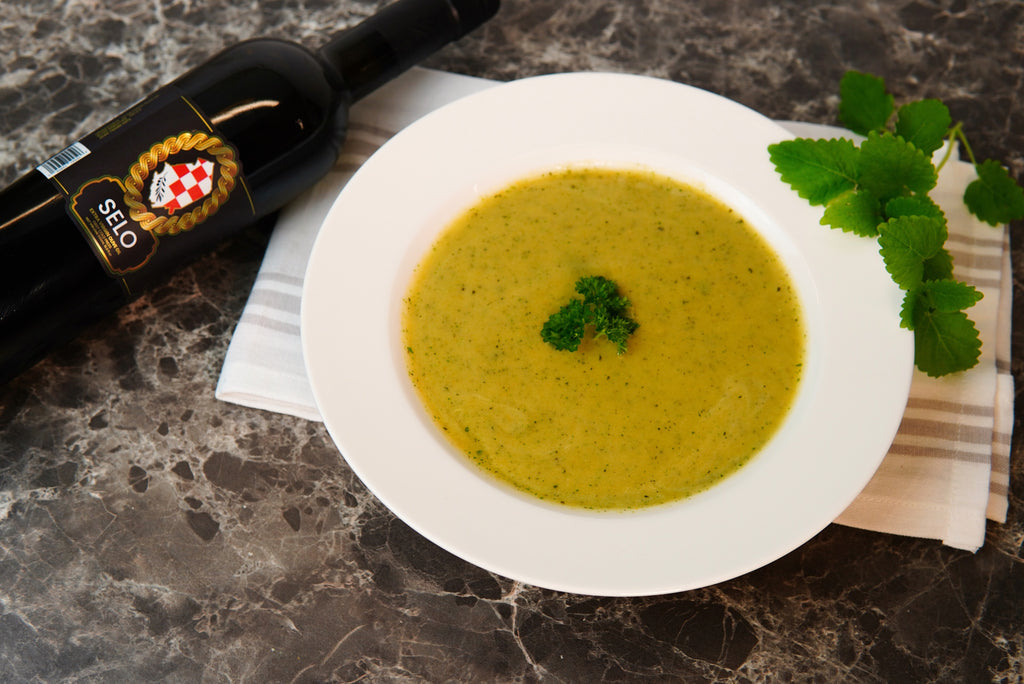 A steaming bowl of Nettle Soup garnished with fresh parsley, accompanied by slices of crusty bread on a wooden table.