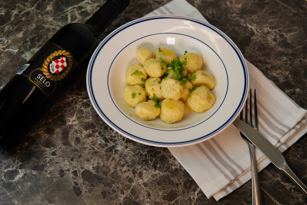 Golden-brown potato dumplings drizzled with melted butter and olive oil, garnished with fresh herbs on a serving dish.