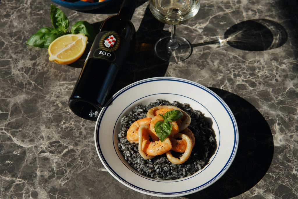 Freshly cooked Black Risotto garnished with parsley, served in a white bowl with a silver spoon on a dark tabletop.