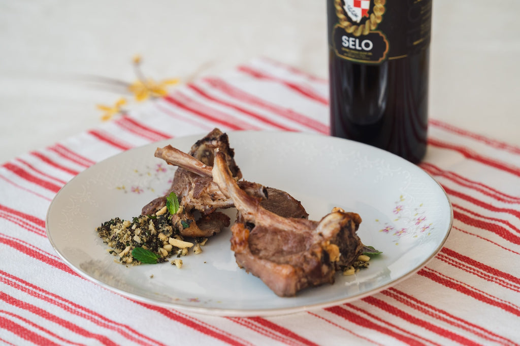 Grilled lamb chops topped with vibrant mint pesto, drizzled with rich Selo Croatian olive oil, and garnished with fresh herbs for a mouthwatering Mediterranean meal.