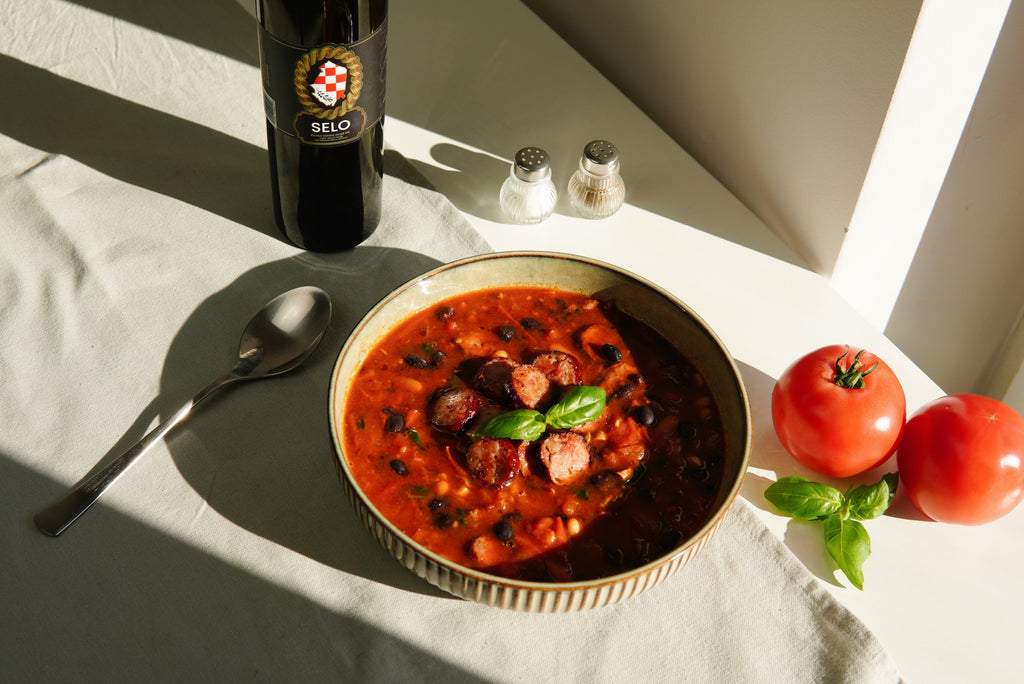 Steaming bowl of Bean and Sausage Soup (Grah s Kobasicom) drizzled with golden Croatian olive oil, evoking the authentic flavors of Croatia.
