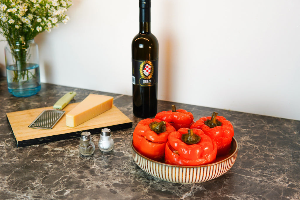 Hearty Croatian stuffed red bell peppers with a golden olive oil drizzle, served on a rustic white plate, embodying the warmth of Mediterranean cuisine.